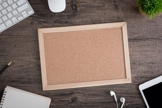 The office desk flat lay view with keyboard, mouse, tree, book, office pin board and earphone on wood texture background.