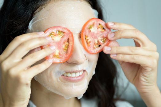 A beautiful woman wearing a towel and a white bathrobe has mask on face-covering eyes with sliced tomatoes with happy and relaxing on the bed at a condominium in the morning.