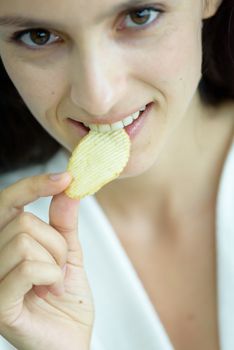 A beautiful woman wearing a towel and a white bathrobe has to eat a snack potato with happy and relaxing on the bed at a condominium in the morning.