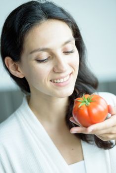 A beautiful woman wearing a towel and a white bathrobe has to prepare to eat tomato with happy and relaxing on the bed at a condominium in the morning.