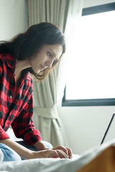 Beautiful woman working on a laptop with smiling and sitting on the bed at a condominium in the morning.