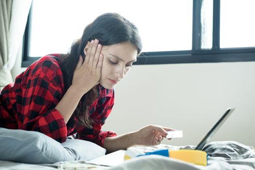 A beautiful woman has lain down on the bed at a condominium and shopping online on a laptop by the credit card with unhappy and worried in the morning.