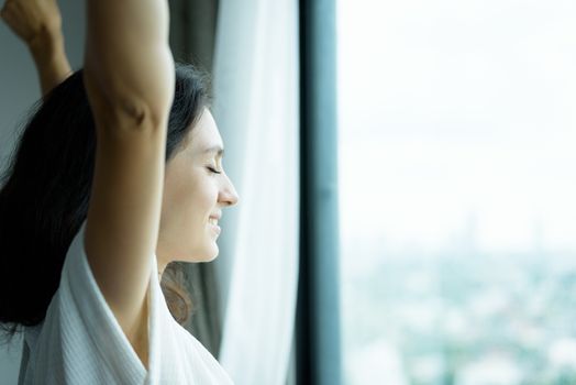 A beautiful woman wearing a towel and a white bathrobe with happy and relaxing on the bed at a condominium in the morning.