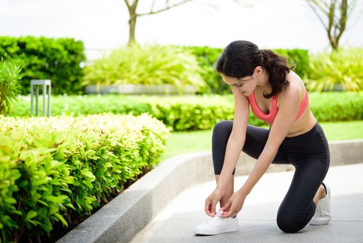 Beautiful woman runner has to tie white shoelaces in the garden.