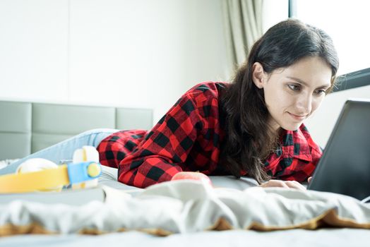 Beautiful woman working on a laptop and lying down on the bed at a condominium in the morning.