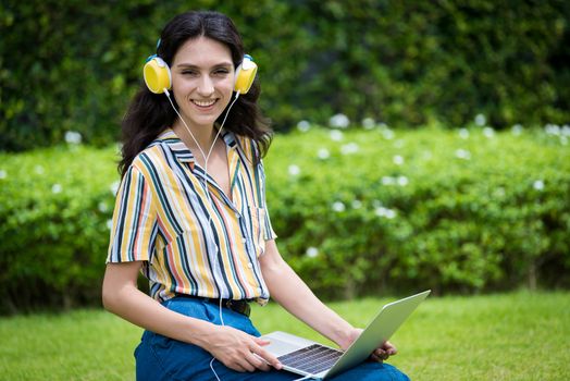 Portrait of a beautiful woman has to listen to music and playing laptop with smiling and relax in the garden.