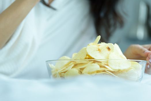 A beautiful woman eating snack potato and playing laptop with lying down on the bed and happiness at a condominium in the morning.