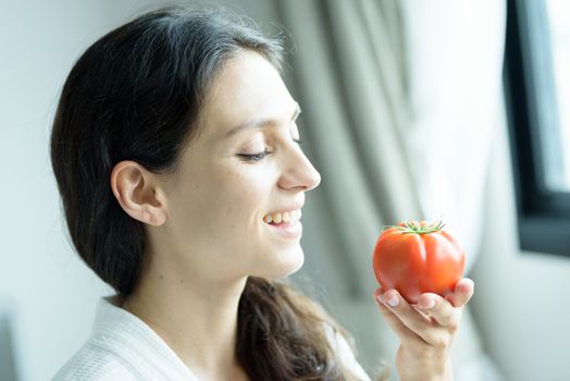 A beautiful woman wearing a towel and a white bathrobe has to prepare to eat tomato with happy and relaxing on the bed at a condominium in the morning.