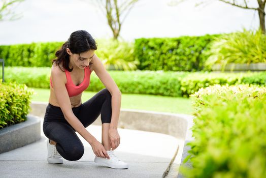 Beautiful woman runner has to tie white shoelaces in the garden.