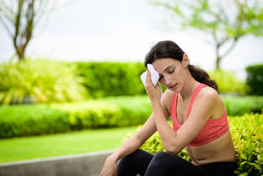 Beautiful woman runner has used a white towel wipe her face after running in the garden.