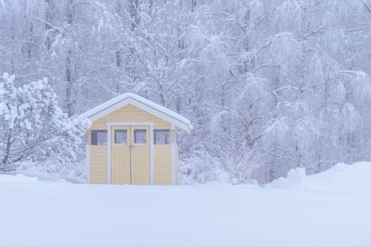 The yellow house in the forest has covered with heavy snow and bad sky in winter season at Tuupovaara, Finland.