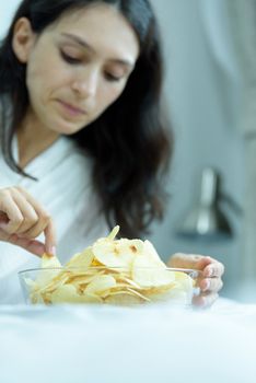 A beautiful woman eating snack potato and playing laptop with lying down on the bed and happiness at a condominium in the morning.