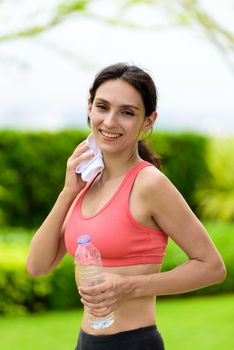 Beautiful woman runner has tired and rest for drinking water and a white towel to wipe her face after running in the garden.