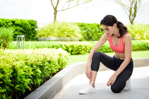 Beautiful woman runner has to tie white shoelaces in the garden.