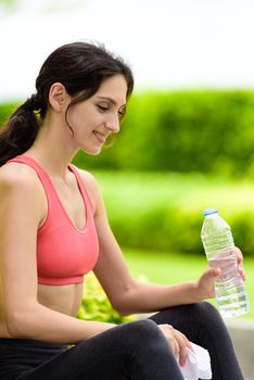 Beautiful woman runner has tired and rest for drinking water and a white towel to wipe her face after running in the garden.