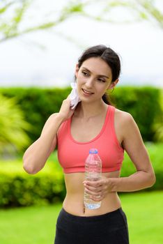 Beautiful woman runner has tired and rest for drinking water and a white towel to wipe her face after running in the garden.