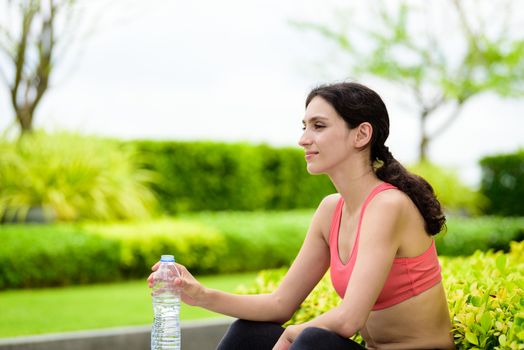 Beautiful woman runner has tired and rest for drinking water after running in the garden.