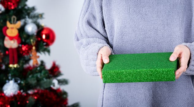 Hands holding a green glitter wrapping paper Christmas gift to surprise with Christmas tree background.