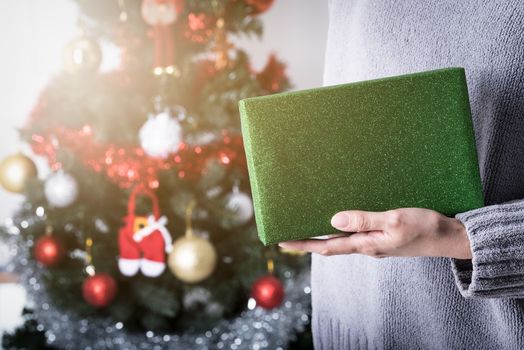 Hand holding a green glitter wrapping paper Christmas gift to surprise with Christmas tree background.