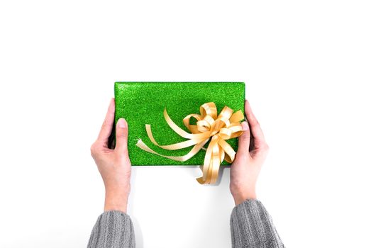 Holding Christmas present with green glitter wrapping paper and gold ribbon isolated on white background.