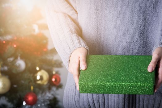 Hands holding a green glitter wrapping paper Christmas gift to surprise with Christmas tree background.