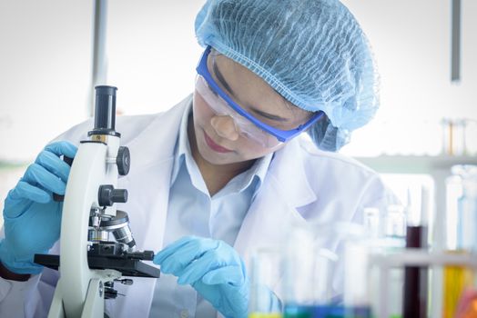 Asian yound student scientist researching with a microscope in a laboratory.