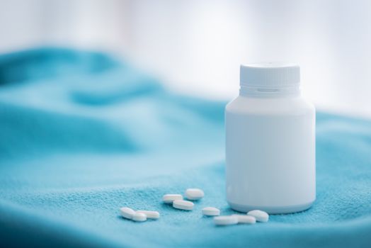 A white medicine bottle and medicine drop on the green bed sheet.