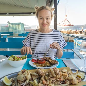 Beautiful female tourist eating delicious sea food on summer vacation in traditional croatian costal restorant by the sea.
