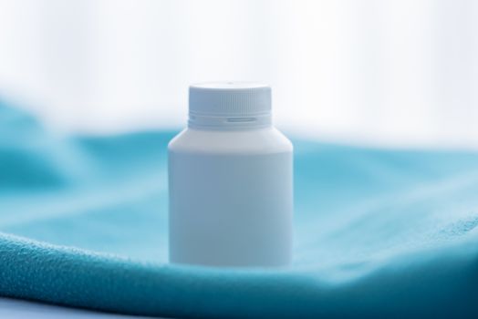 A white medicine bottle on the green bed sheet.