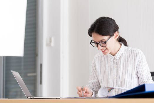 A businesswoman wearing glasses working with smiling and happiness at the office.