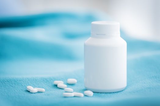 A white medicine bottle and medicine drop on the green bed sheet.