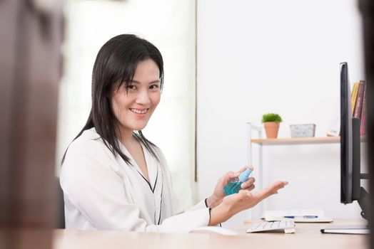 A beautiful Asian businesswoman cleaning hands by cleaner gel to protect COVID-19 before start working from home with safety and happiness.