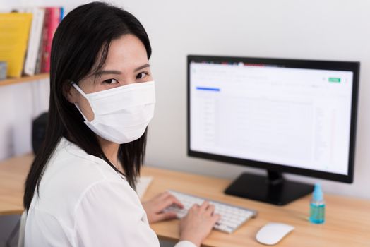 A beautiful Asian businesswoman wearing a mask and cleaner gel to protect COVID-19 before start working from home with safety and happiness.