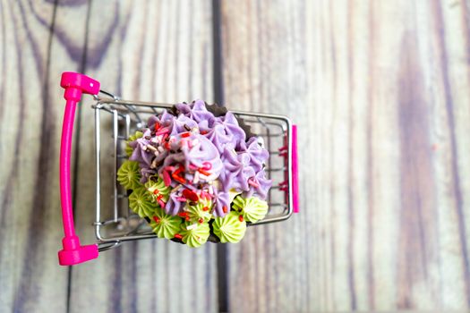 Top down shot of beautifully iced cupcake with green and purple icing on shopping cart on a wooden background. Shows the skills and hobbies people are learning during the coronavirus pandemic