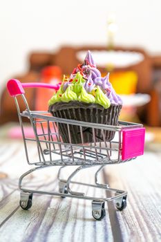 Beautifully iced cupcake with purple frosting and black chocolate base on a shopping cart on a wooden floor with blurred out background. Shows hobbies and skills people are leanring in the coronavirus pandemic