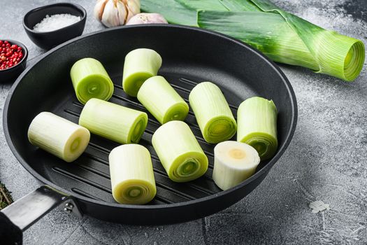 Raw chopped Leeks on grill pan uncooked with herbs ingredients , on textured grey background side view selective focus with space for text