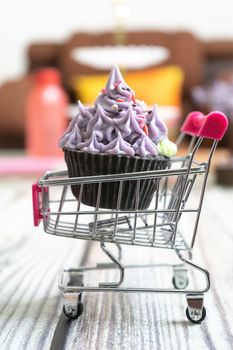 Beautifully iced cupcake with purple frosting and black chocolate base on a shopping cart on a wooden floor with blurred out background. Shows hobbies and skills people are leanring in the coronavirus pandemic