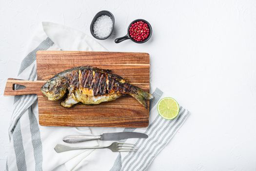 Grilled sea bream or dorado raw fish on chopping board with ingredients over textured white background, top view with space for text