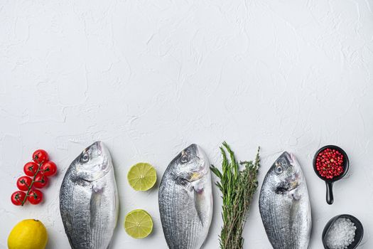 Raw three sea bream or Gilt head bream dorada fish with herbs pepper lime tomato for cooking and grill on white background, top view with space for text