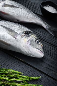 Raw whole pair dorado or sea bream fish with herbs for grill uncooked on black wooden table side view