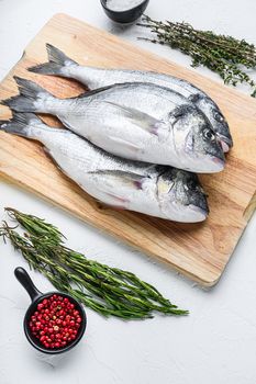Dorado or seabream fish set on chopping board with herbs for grill uncooked on white textured background side view