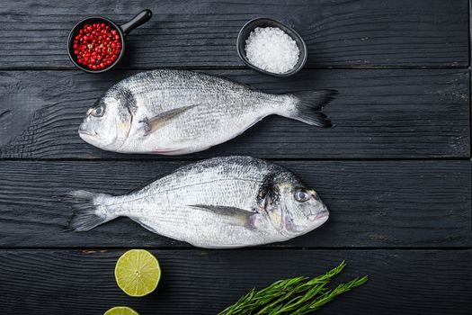 Raw whole pair dorado or sea bream fish with herbs for grill uncooked on black wooden table top view with space for text