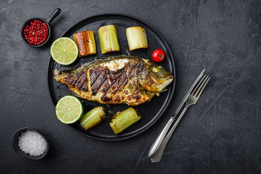 Grilled sea bream or dorado raw fish on black plate with Braised Leeks over textured black background, top view