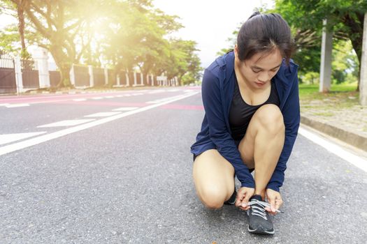 Young woman runner tying laces her shoelaces.  Asian women tying her black shoe.  Woman wear running shoe on to walking park. Healthy and fitness concept. With copy space.