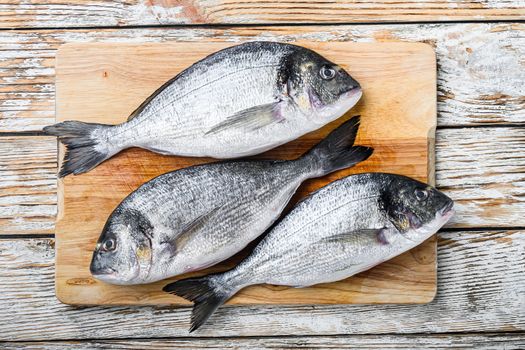 Raw dorada or sea bream on choppong board over white wood table top view
