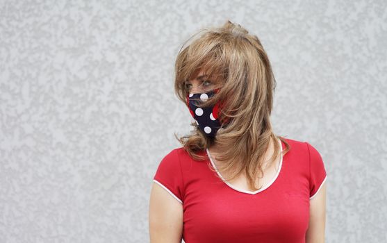 Girl in a protective mask against coronavirus on a background of a gray concrete wall. Primary red color