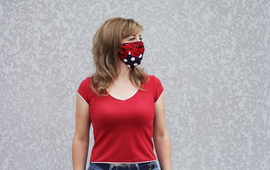 Girl in a protective mask against coronavirus on a background of a gray concrete wall. Primary red color