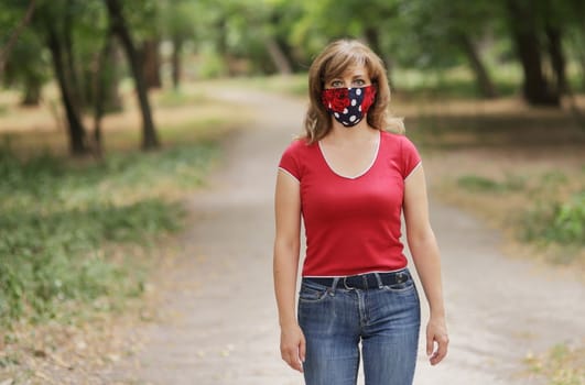 Girl in a protective mask against coronavirus in the park. Primary red color