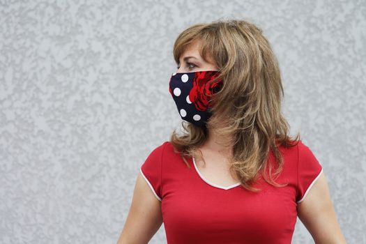 Girl in a protective mask against coronavirus on a background of a gray concrete wall. Primary red color