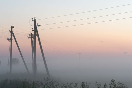 electric poles with wires in the fog in summer, beautiful nature around